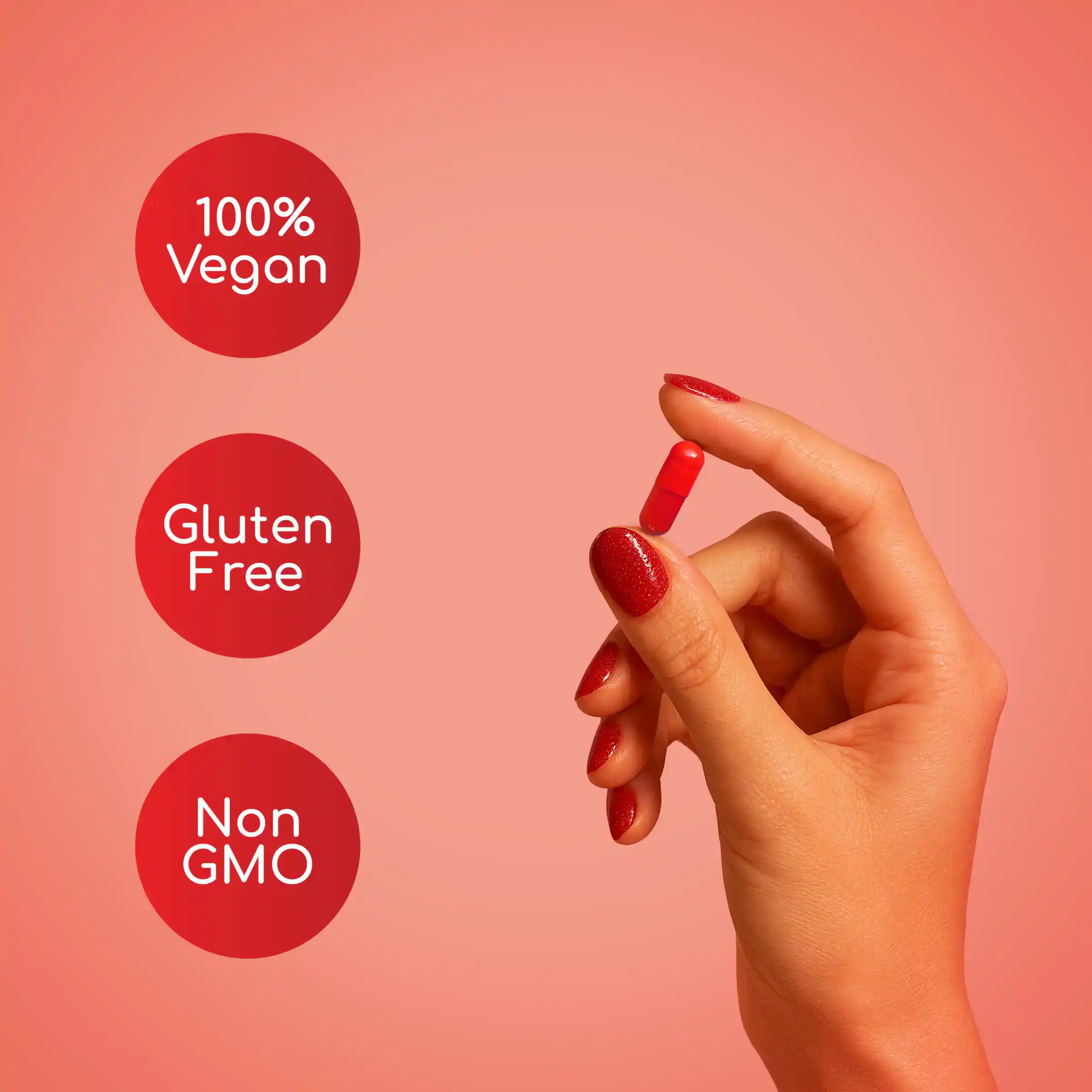 Hand holding a red supplement pill with '100% Vegan', 'Gluten Free', and 'Non GMO' labels on a pink background.